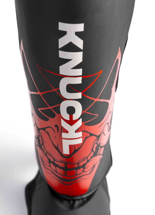 Close-up of Knuckl logo over red Oni design on shin guard